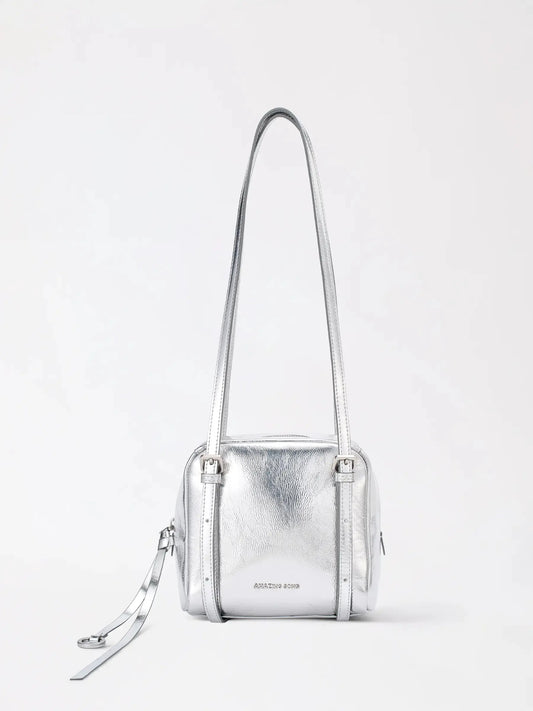A small square boxy leather bag with a wraparound zip top, a tassel pull and adjustable shoulder straps