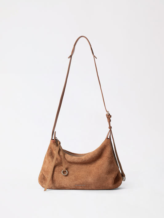Large suede donut hobo bag in tan resting on a bar counter beside a phone and lipstick