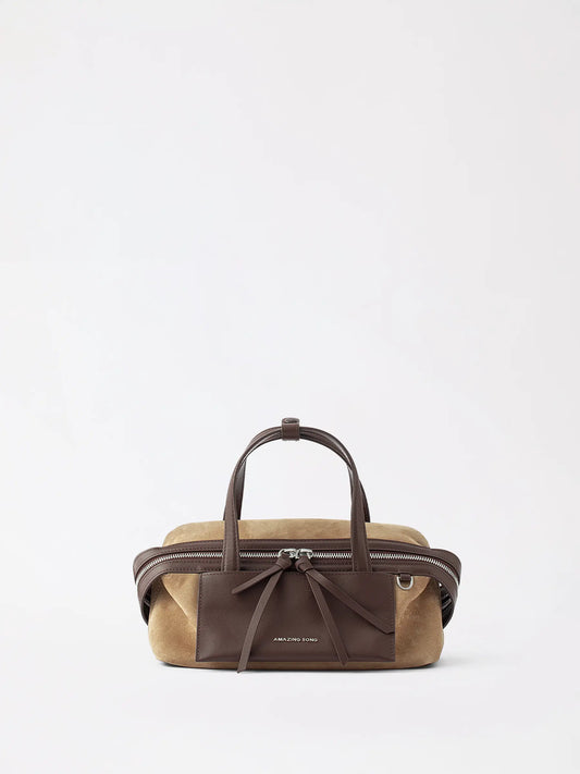 A small cheese-roll pillow bag in warm tan top-grain leather resting on a knit throw
