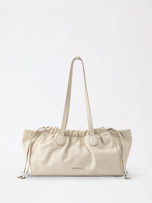 A large soft cloud-shaped hobo bag in warm tan leather resting on a linen shelf
