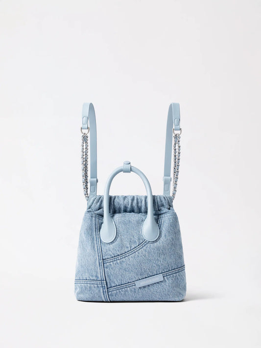 A small denim hobo backpack with tan leather trim on a pale linen chair