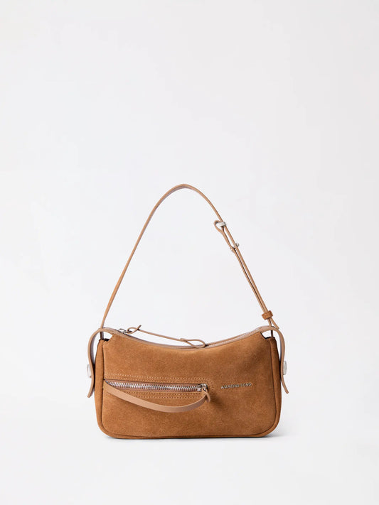 A soft suede mahjong-shaped leather bag in warm tan resting on a knit throw