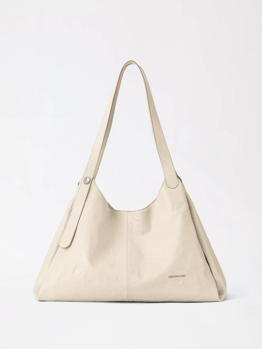 A berry-shaped top-grain leather tote bag in deep burgundy standing on a marble counter
