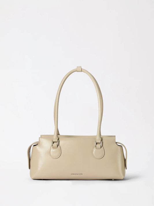 A plump padded leather pillow pack bag in warm tan leather resting on a wooden table
